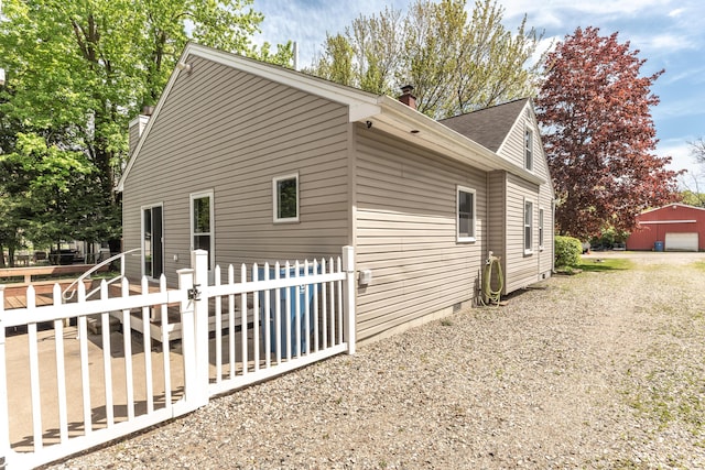 view of property exterior with a chimney, fence, a gate, a detached garage, and a shingled roof