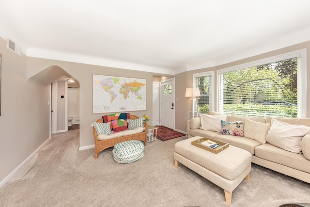 living area with arched walkways, baseboards, and carpet floors