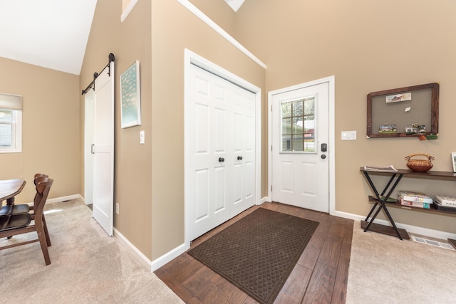 foyer entrance featuring a barn door, wood finished floors, baseboards, and high vaulted ceiling