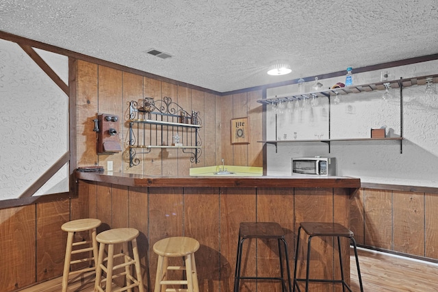 2394 Cedar Crest Dr NE, Grand Rapids, MI 49525 - indoor wet bar featuring a textured ceiling, stainless steel microwave, wooden walls, and wood finished floors