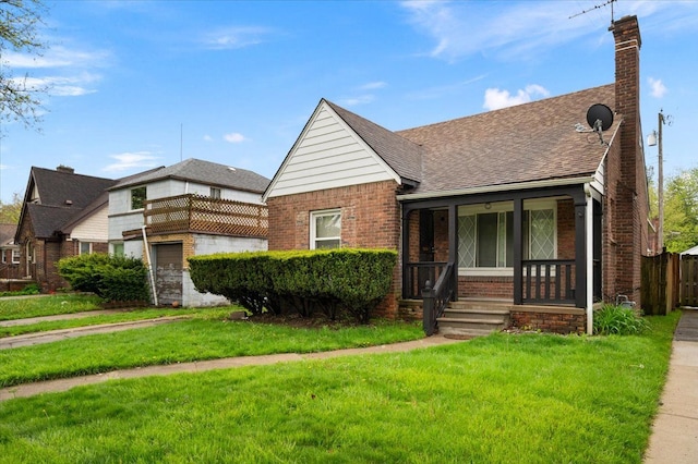 view of front facade with brick siding, a front lawn, covered porch, a chimney, and roof with shingles