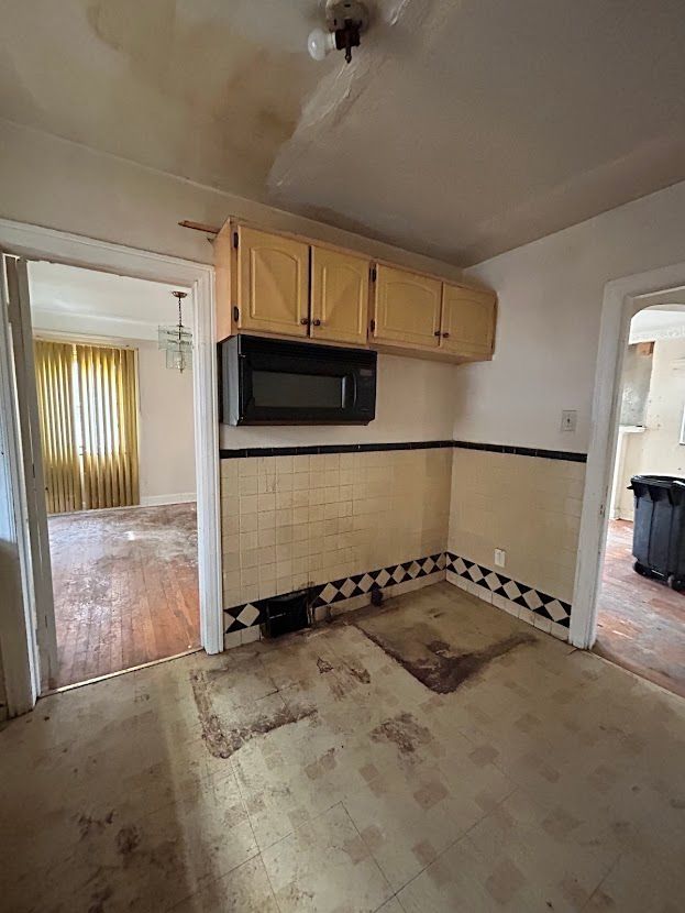 kitchen featuring black microwave, a wainscoted wall, and light brown cabinetry