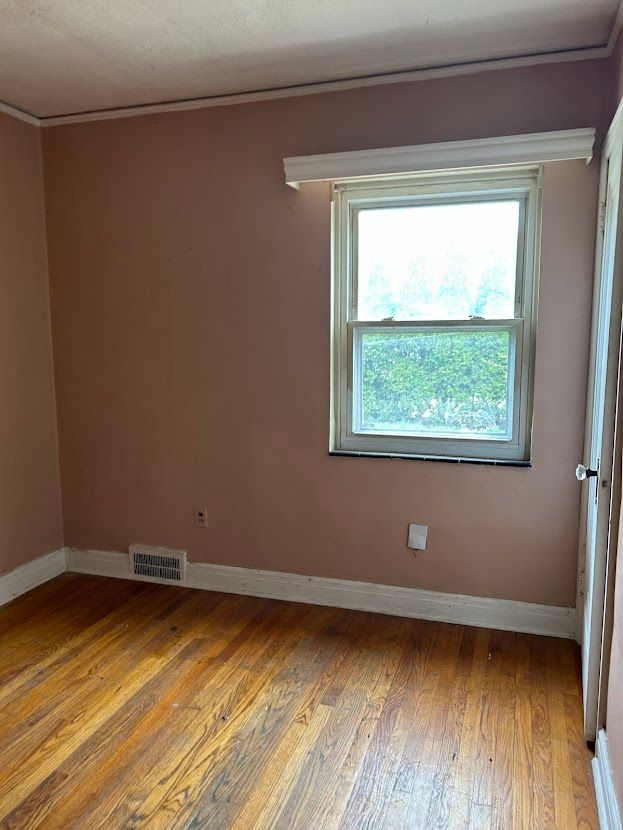 unfurnished room featuring hardwood / wood-style flooring, healthy amount of natural light, baseboards, and crown molding
