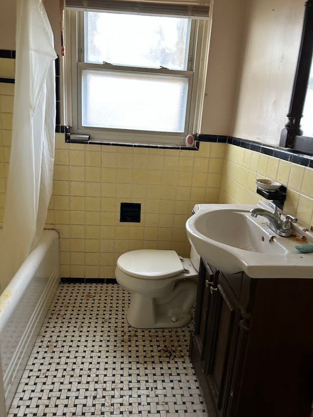 full bath featuring tile walls, vanity, healthy amount of natural light, toilet, and a wainscoted wall