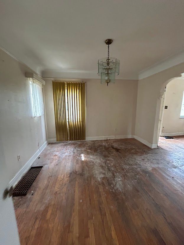 unfurnished dining area with wood-type flooring, arched walkways, baseboards, crown molding, and a chandelier