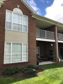 back of house with a balcony, brick siding, a lawn, and a patio area