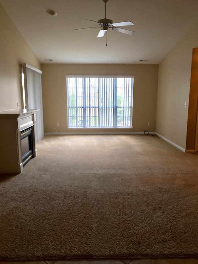 unfurnished living room with a ceiling fan, baseboards, a glass covered fireplace, and light colored carpet