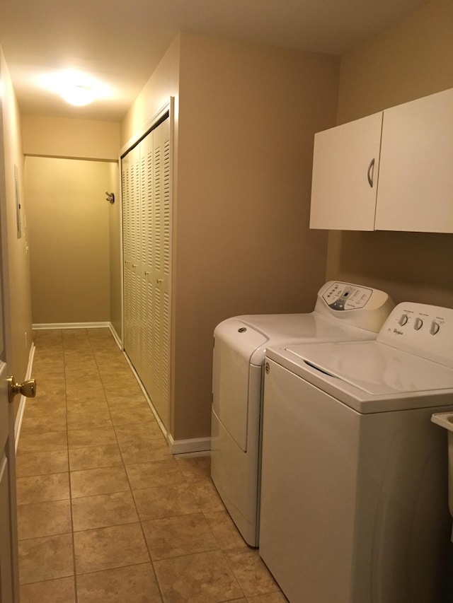 laundry area featuring washer and clothes dryer, cabinet space, light tile patterned flooring, and baseboards