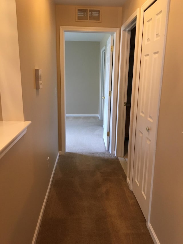 corridor featuring dark colored carpet and baseboards