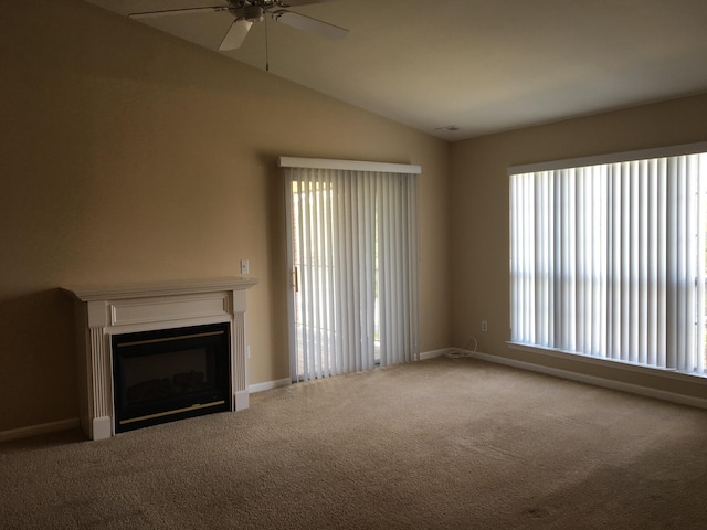 unfurnished living room featuring a ceiling fan, carpet flooring, vaulted ceiling, baseboards, and a glass covered fireplace