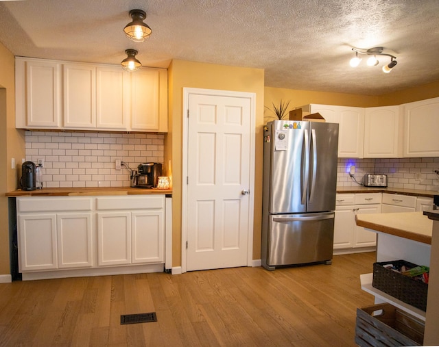 kitchen with freestanding refrigerator, white cabinets, light wood-type flooring, backsplash, and a textured ceiling