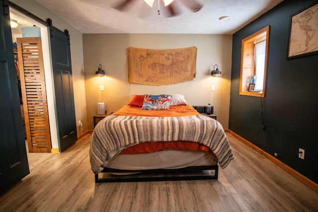 bedroom featuring a barn door, wood finished floors, baseboards, and ceiling fan