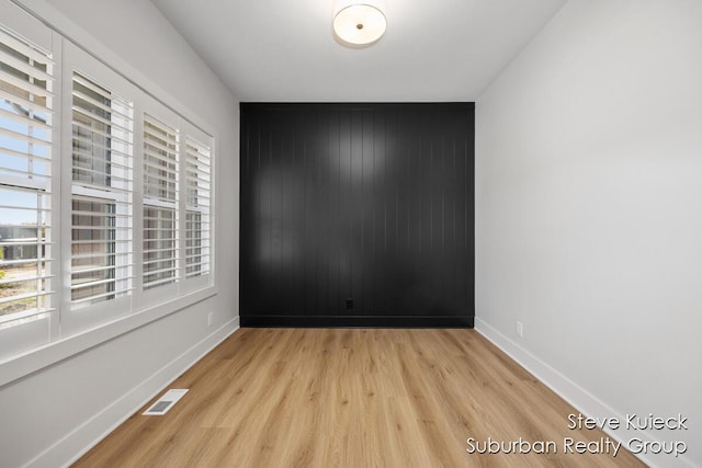 unfurnished room featuring wood finished floors, baseboards, and an accent wall