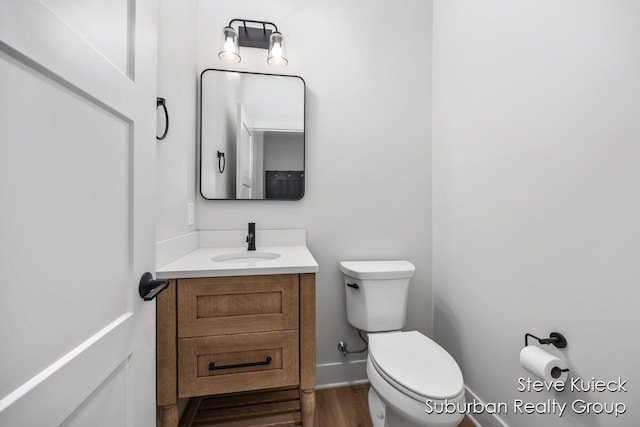 bathroom with toilet, vanity, baseboards, and wood finished floors