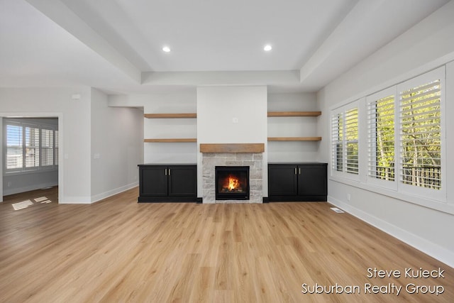 unfurnished living room featuring a fireplace, light wood-type flooring, baseboards, a tray ceiling, and recessed lighting