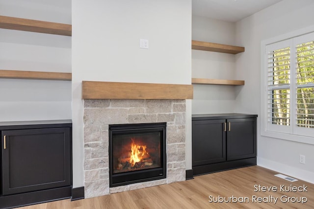 detailed view of wood finished floors, a glass covered fireplace, and baseboards