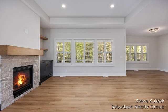 unfurnished living room with a glass covered fireplace, baseboards, light wood finished floors, recessed lighting, and a raised ceiling