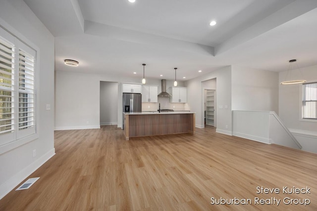 kitchen with stainless steel fridge with ice dispenser, wall chimney range hood, open floor plan, light countertops, and light wood-type flooring