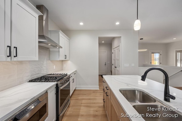 kitchen with appliances with stainless steel finishes, a sink, wall chimney exhaust hood, light wood-style floors, and tasteful backsplash