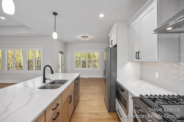 kitchen with wall chimney range hood, appliances with stainless steel finishes, a sink, recessed lighting, and light wood finished floors