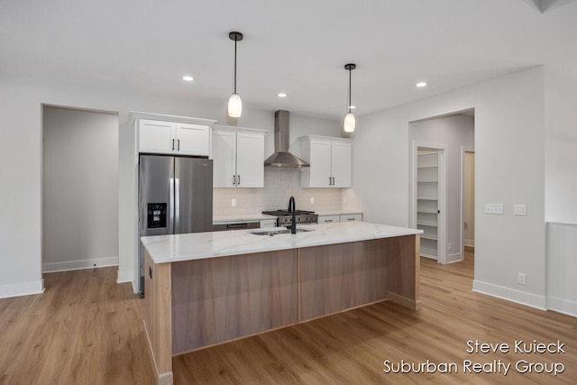 kitchen with wall chimney exhaust hood, white cabinetry, decorative backsplash, light wood-style floors, and an island with sink