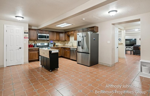 kitchen with appliances with stainless steel finishes, a sink, light countertops, decorative backsplash, and a kitchen island