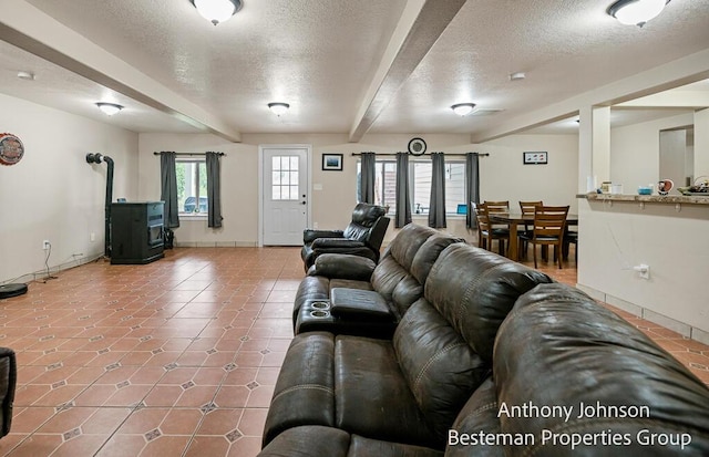 tiled living room with a textured ceiling, a wood stove, baseboards, and beamed ceiling