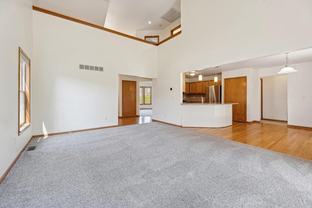 unfurnished living room with light colored carpet, baseboards, and a towering ceiling