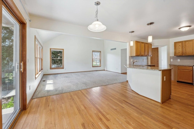 kitchen with brown cabinetry, light wood finished floors, open floor plan, hanging light fixtures, and lofted ceiling