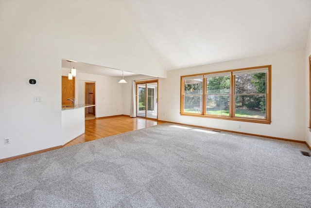 unfurnished room featuring light carpet, baseboards, high vaulted ceiling, and a sink