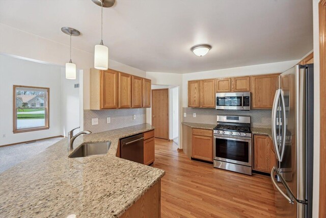 kitchen with appliances with stainless steel finishes, a sink, a peninsula, tasteful backsplash, and light stone counters