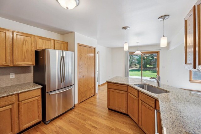 kitchen with freestanding refrigerator, a sink, light wood-type flooring, pendant lighting, and backsplash