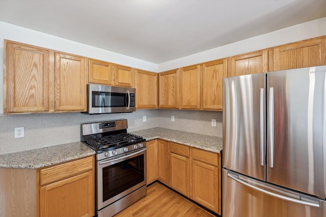 kitchen featuring stainless steel appliances, backsplash, light stone counters, and light wood-type flooring