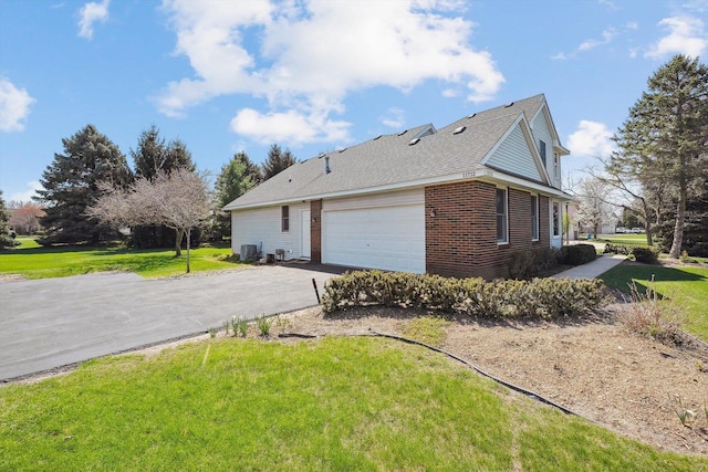 view of property exterior with a garage, brick siding, a lawn, and cooling unit