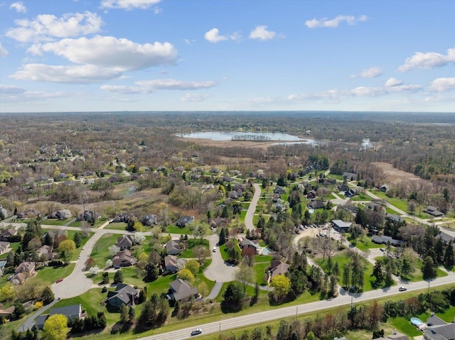 aerial view of property and surrounding area featuring a heavily wooded area, a nearby body of water, and nearby suburban area