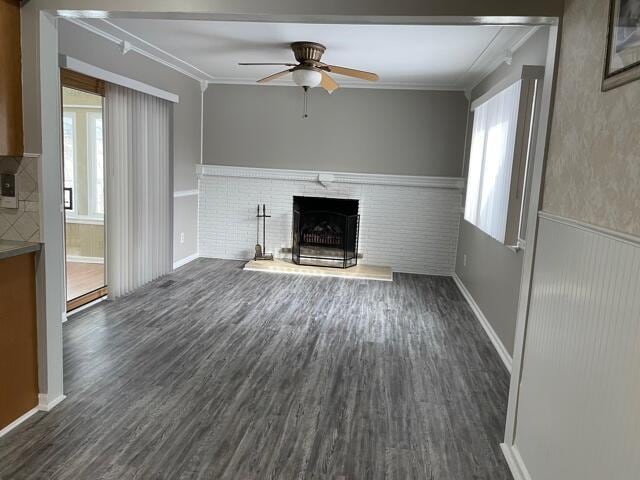 unfurnished living room with healthy amount of natural light, ornamental molding, a brick fireplace, and dark wood-type flooring