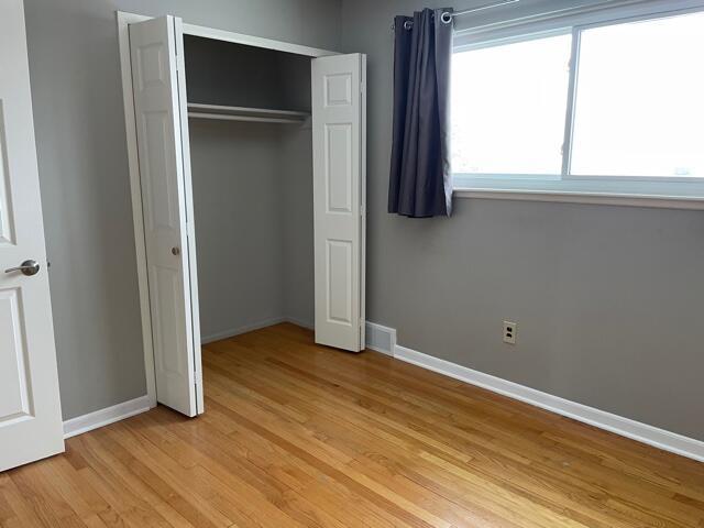 unfurnished bedroom featuring light wood-style flooring, a closet, and baseboards