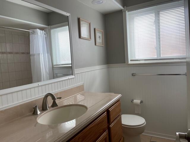 full bathroom featuring vanity, toilet, a wainscoted wall, tile patterned flooring, and curtained shower
