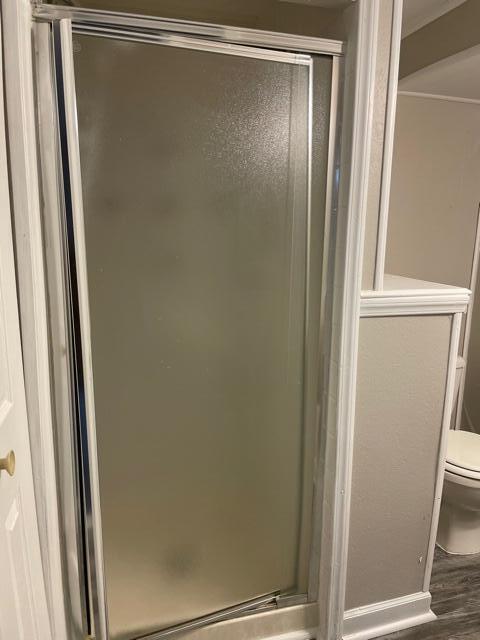 bathroom with toilet, a shower stall, and wood finished floors
