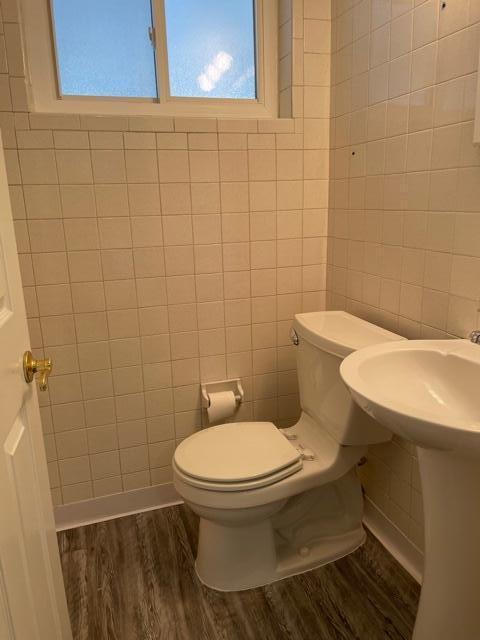 bathroom featuring wood finished floors, toilet, and tile walls