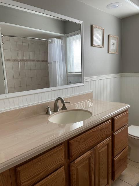 bathroom with toilet, wainscoting, tile patterned flooring, vanity, and curtained shower