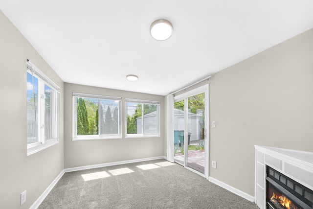unfurnished living room with carpet floors, a glass covered fireplace, and baseboards