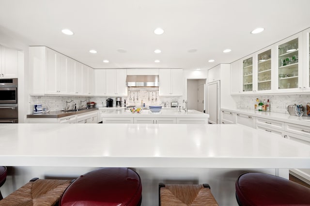 50102 Alpine Blvd, New Buffalo, MI 49117 - kitchen with a breakfast bar, a sink, decorative backsplash, wall chimney exhaust hood, and recessed lighting