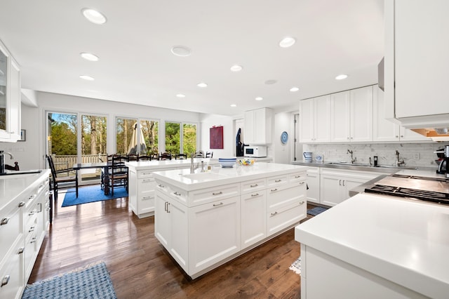 50102 Alpine Blvd, New Buffalo, MI 49117 - kitchen featuring an island with sink, white microwave, decorative backsplash, white cabinets, and light countertops