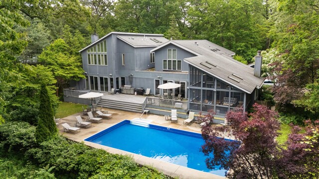 50102 Alpine Blvd, New Buffalo, MI 49117 - rear view of property featuring a sunroom, a chimney, a wooden deck, an outdoor pool, and a patio