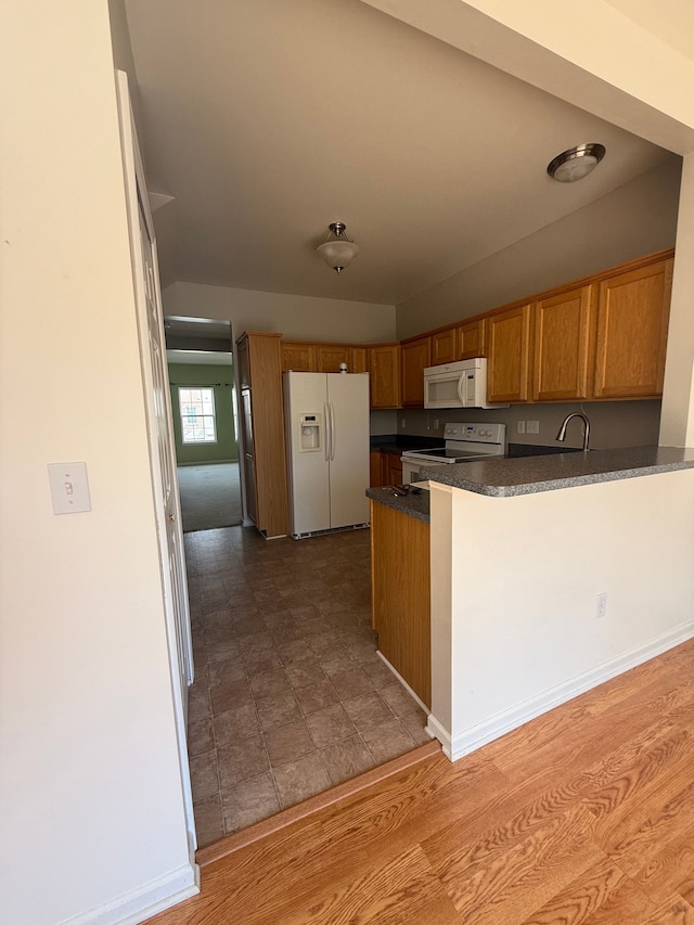 kitchen with white appliances, brown cabinets, dark countertops, a peninsula, and a sink