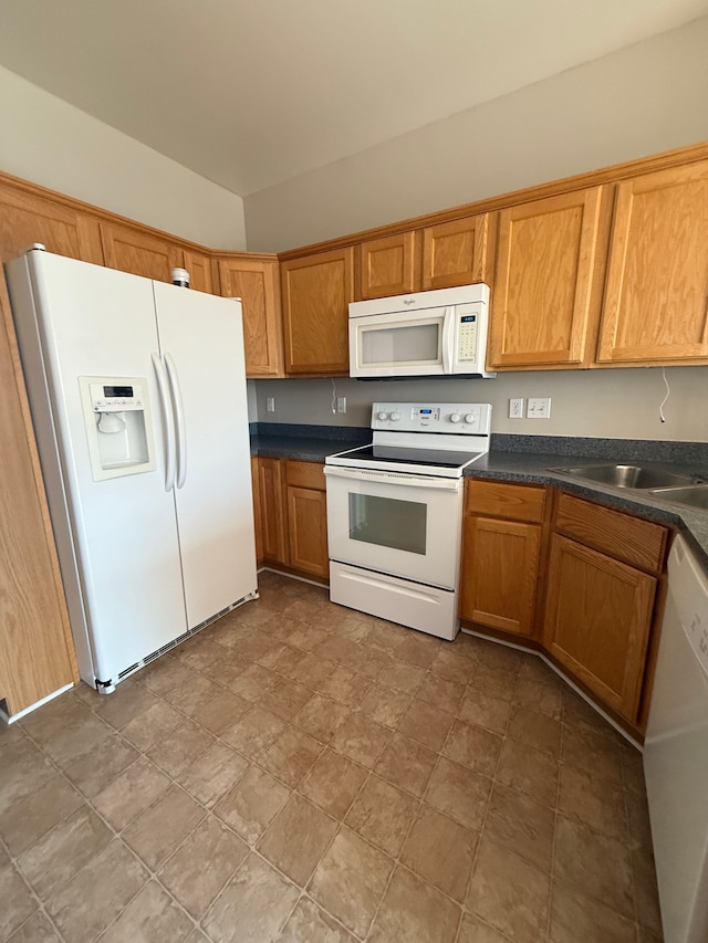 kitchen featuring white appliances, dark countertops, a sink, brown cabinetry, and stone finish floors