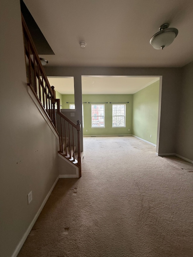 unfurnished living room with carpet, baseboards, and stairs