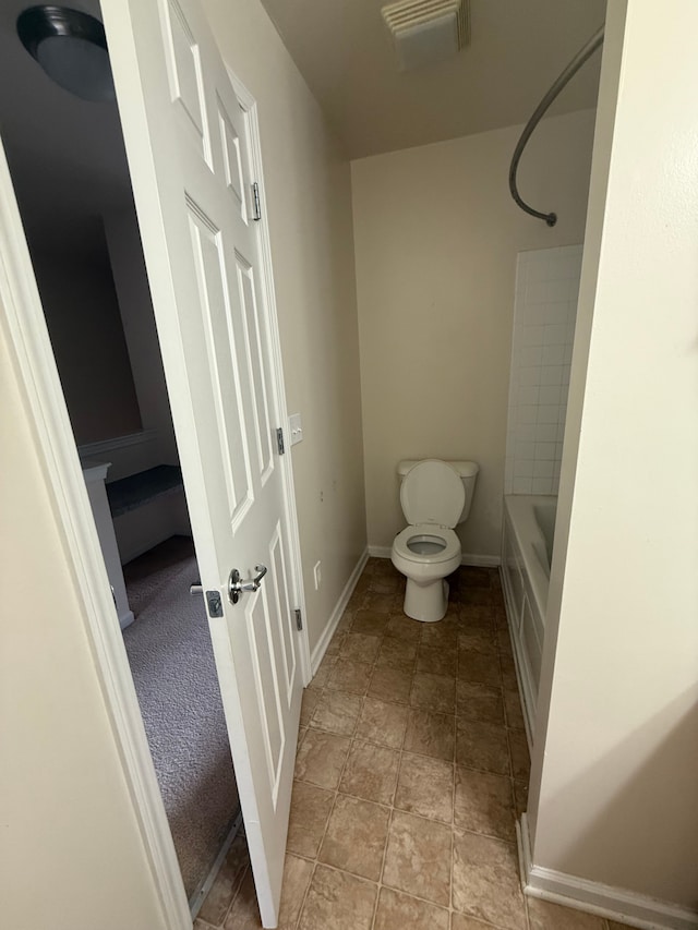 bathroom with baseboards, toilet, shower / bathtub combination, and stone finish floors