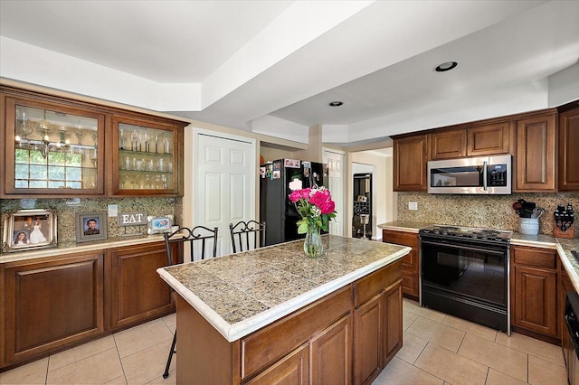 15672 Robert Dr, Macomb, MI 48044 - kitchen featuring black appliances, a kitchen island, light tile patterned flooring, tasteful backsplash, and glass insert cabinets